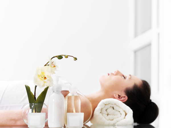 A woman relaxes in a serene medspa with an orchid, a white candle, and skin care products in the foreground